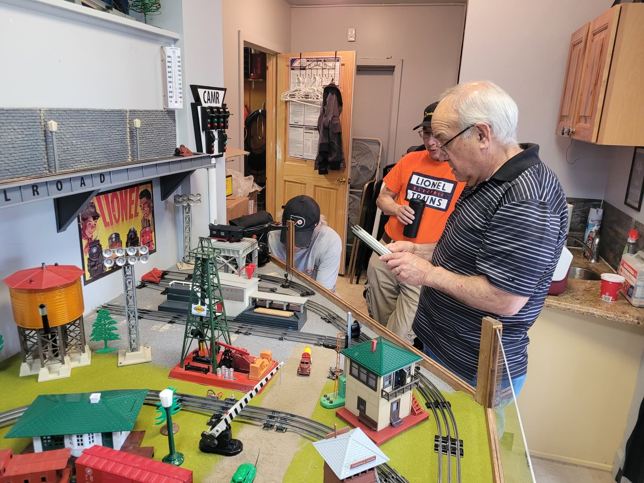 Club members examining a detailed Lionel model train layout with miniature buildings, water tower, and crossing gates